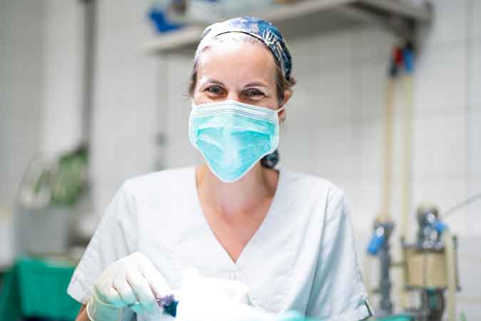 Eine lächelnde Tierärztin trägt OP-Kleidung, Haube und Maske.